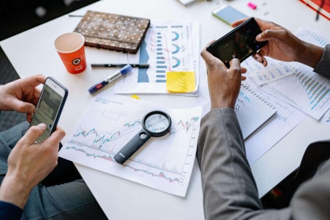 Visão de cima mostrando celular com app financeiro, planilha de gastos e caderno para rastreamento de despesas.